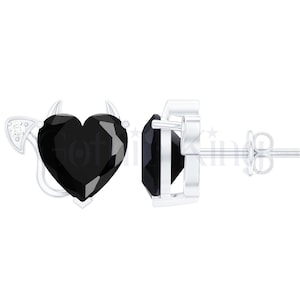 May include: A pair of silver stud earrings. Each earring features a heart-shaped black gemstone with small horns and a tail design. The earrings are displayed on a white background.