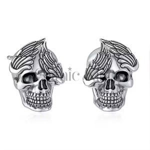 Könnte beinhalten: Ein Paar silberne Totenkopf-Ohrringe mit Engelsflügeln, die ein Auge bedecken. Die Flügel sind detailliert und kunstvoll.
