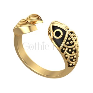 Può includere: Anello in oro con un design a forma di pesce nero. Il pesce ha un occhio nero con un piccolo punto dorato al centro.