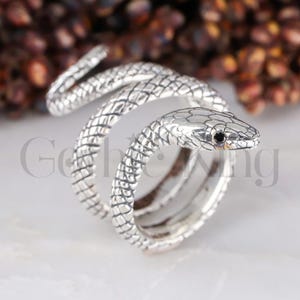 May include: A silver snake ring with a coiled design. The snake's head features scale detailing and a black eye. The ring wraps around the finger multiple times, creating a unique accessory. A stylish piece of jewellery.