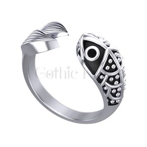 Può includere: Anello d'argento con un design a forma di pesce nero. Il pesce ha un occhio nero e un motivo dettagliato di squame. L'anello è aperto da un lato e ha una fascia liscia.