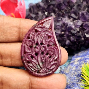 May include: A carved ruby pendant in the shape of a teardrop with a floral design. The pendant is a deep red colour and has a high polish.