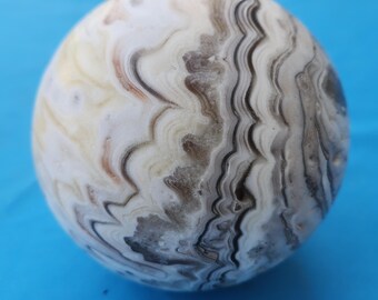May include: A white, gray, and brown agate sphere with swirling patterns. The sphere is smooth and polished.