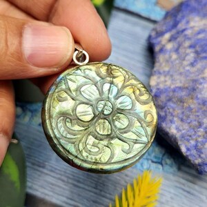 May include: A silver pendant with a round, green and blue labradorite stone featuring a carved floral design.