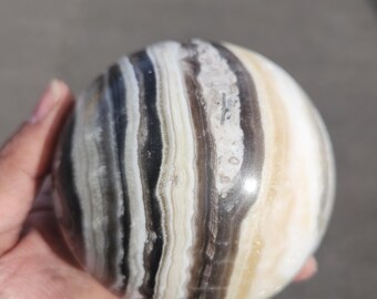 May include: A polished, round, banded agate sphere with white, brown, and black stripes. The sphere is smooth and has a glossy finish.