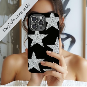 May include: Black phone case with a pattern of large, sparkling silver stars. The case is held up in front of a person's face. The text "MagSafe Compatible" is printed on the upper left corner of the image.