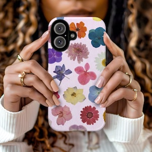 Op de afbeelding: Een roze telefoonhoesje met een bloemenpatroon met geperste bloemen in verschillende kleuren, waaronder roze, blauw, geel en rood.