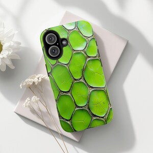 May include: A green phone case with a textured pattern resembling reptile skin. The case has a glossy finish and a black camera cutout. The design features a network of irregular, interconnected shapes in varying shades of green and brown.