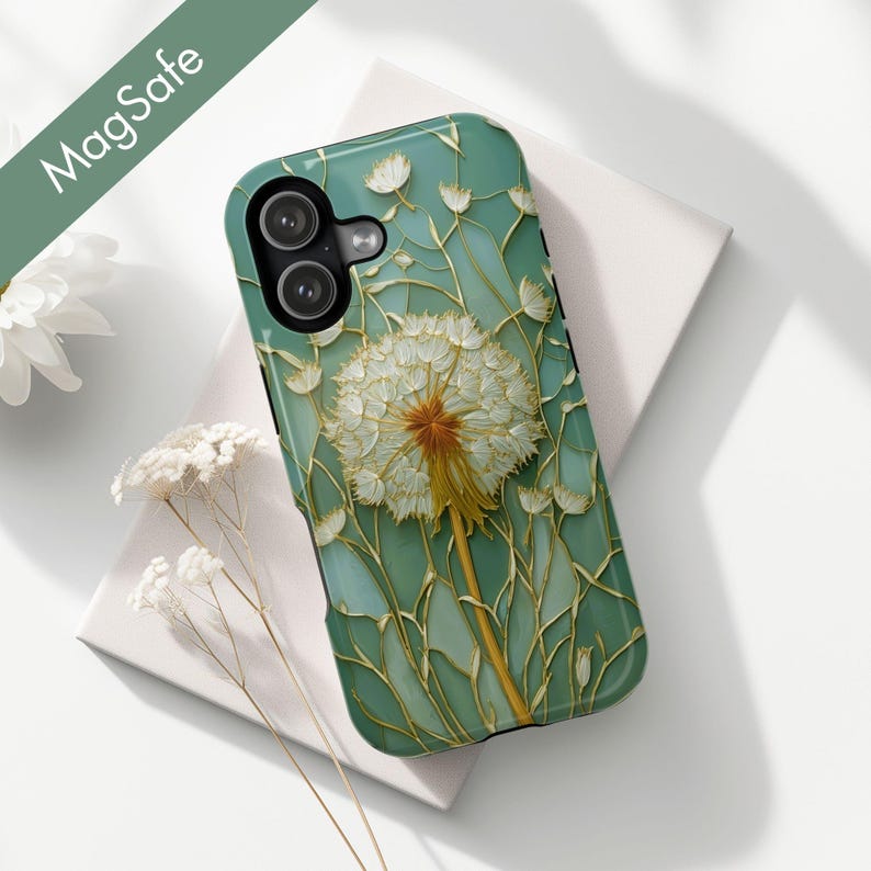 Op de afbeelding: Een turquoise telefoonhoesje met een paardenbloemontwerp. De hoes heeft een grote, gedetailleerde paardenbloem met een witte zaadkop en een gele steel, tegen een achtergrond van gestileerde stelen en kleine witte bloemen. De tekst "MagSafe" is zichtbaar.