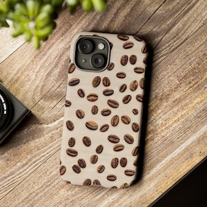 May include: A beige phone case with a pattern of brown coffee beans. The case has a camera lens cutout with three lenses.