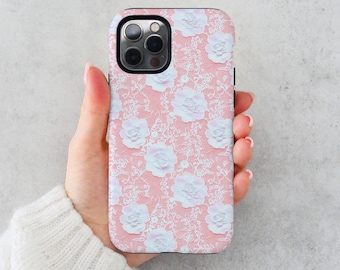May include: A pink phone case with a white lace pattern and white flowers. The case has a cutout for the camera lens.
