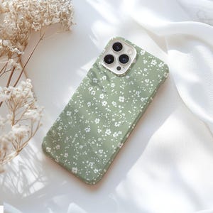 May include: A green phone case with a white floral pattern. The case has a cutout for the camera lens.