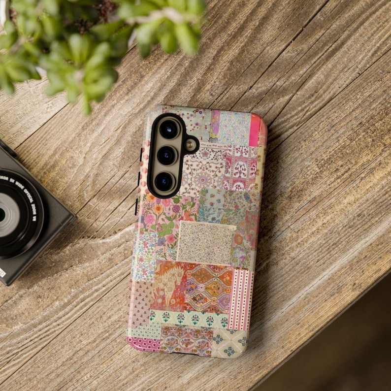 May include: A phone case with a patchwork design featuring various floral and geometric patterns in shades of pink, blue, and green. The case has a cutout for a triple camera lens.