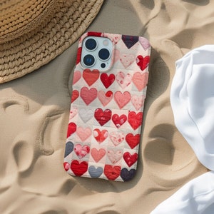 May include: A phone case with a patchwork design featuring a variety of red, pink, and white hearts. The case has a camera lens cutout and a white background.