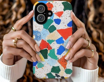 May include: A white phone case with a colorful terrazzo pattern. The case has a camera lens cutout and a white background with green, blue, red, and yellow accents.