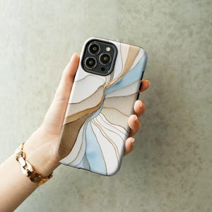 May include: A smartphone case with a swirling abstract design in shades of brown, beige, and light blue, accented with gold lines. The case has a glossy finish and a camera cutout. A gold bracelet is visible in the image.