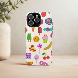 May include: White iPhone case with a colorful pattern of various sweets and treats, including ice cream, cupcakes, candy, and fruit.