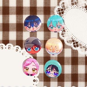 May include: Six circular pin-back buttons featuring stylized anime-style character faces. The buttons display various hair colors including dark blue, teal, brown, blonde, pink, and black, with expressive eyes and distinct facial features on each individual pin.