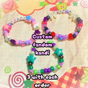 May include: Three colorful kandi bracelets with star and bead accents. One bracelet spells "Mizuki", another "Duran", and the third features green star beads. The image includes the text "Custom fandom kandi" and "3 with each order".