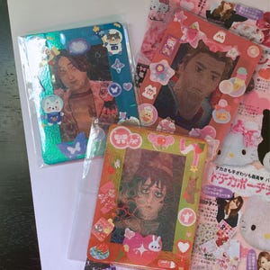 May include: Several decorated photo cards with images of people, surrounded by colorful stickers. The cards are in plastic sleeves. One card has a teal frame with astronaut bear stickers. Another has a red frame with star and bow stickers.