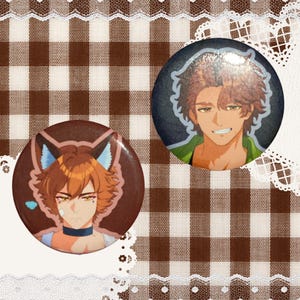 May include: Two circular pin-back buttons featuring anime-style illustrations. One button displays a character with orange hair, fox-like ears, and a blue collar. The second button shows a character with brown hair and a green shirt against a dark background.
