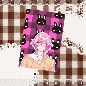 May include: A rectangular print featuring an anime-style character with pink hair, blue eyes, and a tan sweater over a white turtleneck. The background consists of a vibrant pink and dark purple plaid pattern decorated with small black rabbit faces.