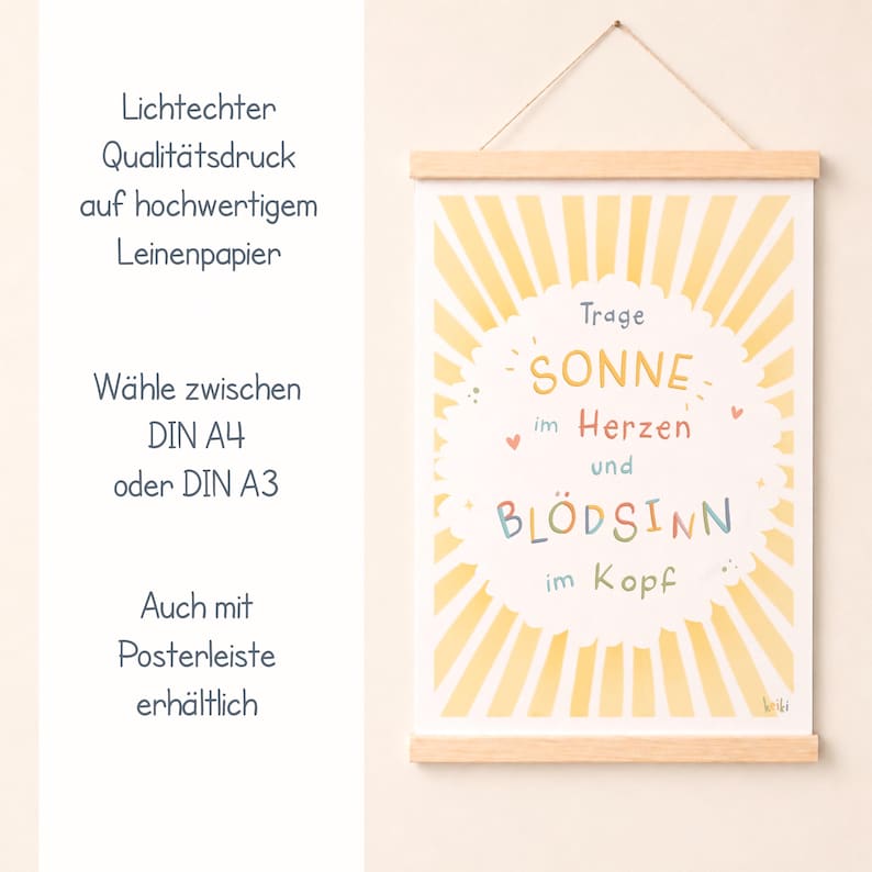 May include: A framed art print with a wooden hanger. The print features a yellow sunburst design with the words "SONNE im Herzen und BL&Ouml;DSINN im Kopf" in colorful lettering. Additional text in German is also present.