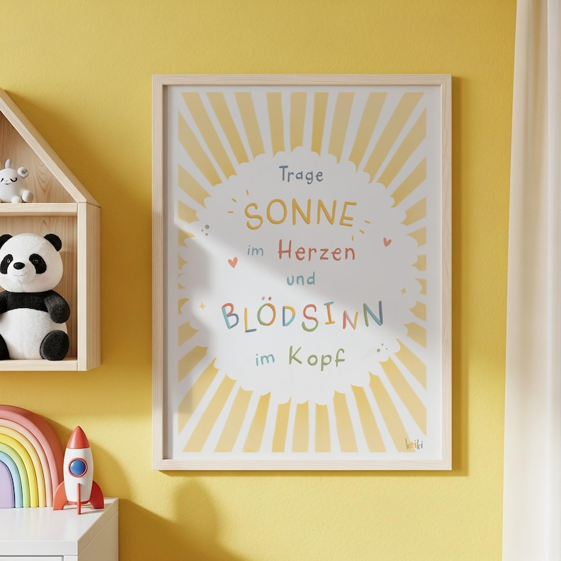 May include: A framed print with a light wood frame. The print features a sunburst design with the words "SONNE im Herzen und BL&Ouml;DSINN im Kopf" in colorful text. The print is on a yellow wall.