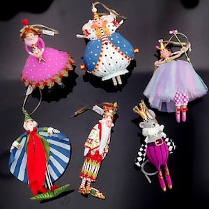 May include: A collection of six whimsical Christmas ornaments. The ornaments feature various characters in colorful costumes, including a queen, a ballerina, and a mouse. Each ornament has a unique design with intricate details and a hanging loop.