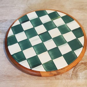 Op de afbeelding: Een ronde houten serveerplank met een groen en wit geblokt patroon. De plank heeft een natuurlijke houten rand en een glanzende afwerking. Deze decoratieve plank is geschikt voor het serveren van hapjes of als decoratief keukenartikel.