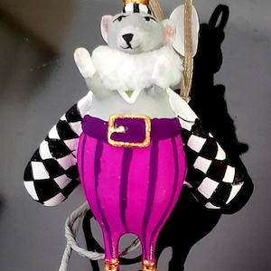 May include: A whimsical ornament of a mouse dressed as a king. The mouse has a gold crown, a white fur collar, and a purple outfit with gold accents. The mouse has black and white checkered wings and pink shoes. A gold string is attached for hanging.