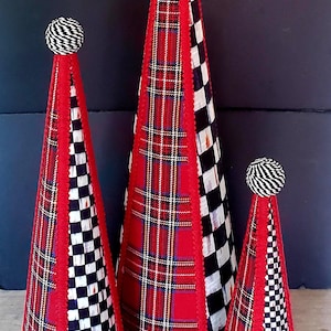 Op de afbeelding: Drie decoratieve kegelvormige objecten. De kegels hebben rode geruite stof, zwart-wit geruite stof en rode randen. Elke kegel is bekroond met een zwart-wit gestreepte bal.