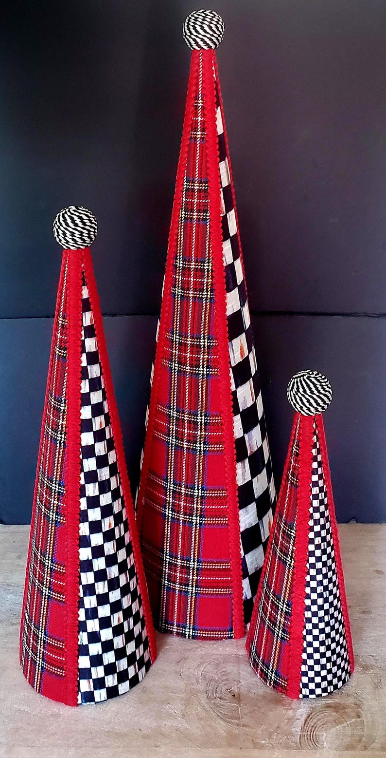 Op de afbeelding: Drie decoratieve kegelvormige objecten. De kegels hebben rode geruite stof, zwart-wit geruite stof en rode randen. Elke kegel is bekroond met een zwart-wit gestreepte bal.