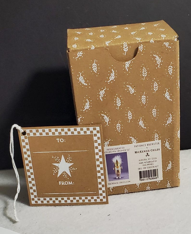 May include: A brown cardboard box and gift tag set with white leaf and dot patterns. The tag reads "TO:" and "FROM:" with a star design. The box has product information and a picture of an ornament.