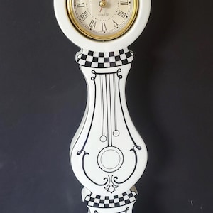 May include: A white quartz clock with a gold-tone bezel and Roman numerals. The clock has a decorative black and white checkered and scrollwork design. The clock is approximately 12 inches tall.