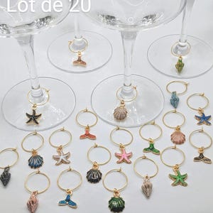 May include: A collection of twenty wine glass charms with gold-colored rings and various sea-themed pendants. Charms include starfish, seashells, and mermaid tails in multiple colors. The text "Lot de 20" is visible in the image.