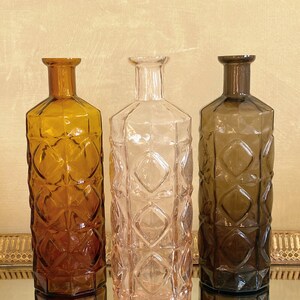 May include: Three glass bottles with a diamond pattern. The bottles are amber, pink, and brown.