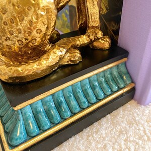 K&ouml;nnte beinhalten: Goldfarbene Leopardenstatue mit strukturierter Oberfl&auml;che, auf einem schwarzen Sockel mit t&uuml;rkisen und goldenen Akzenten. Der Artikel ist ein dekoratives Element f&uuml;r Zuhause oder B&uuml;ro.