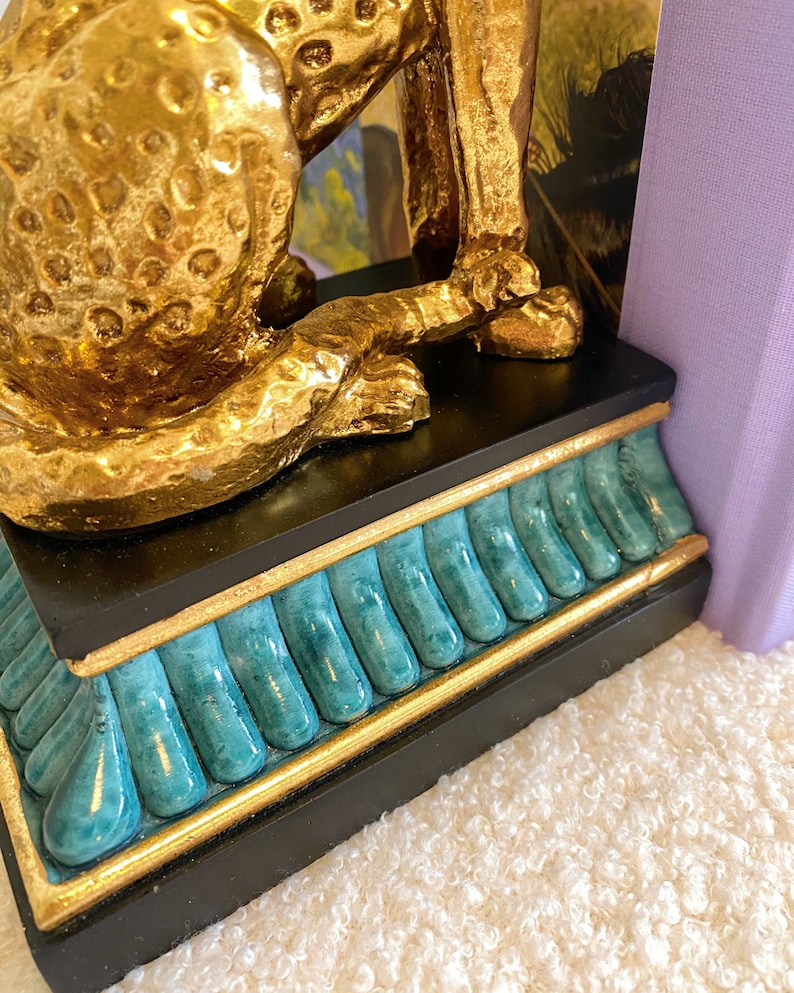 K&ouml;nnte beinhalten: Goldfarbene Leopardenstatue mit strukturierter Oberfl&auml;che, auf einem schwarzen Sockel mit t&uuml;rkisen und goldenen Akzenten. Der Artikel ist ein dekoratives Element f&uuml;r Zuhause oder B&uuml;ro.