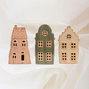 Puede incluir: Tres casas de cerámica con recortes de ventanas. Las casas son en tonos de rosa, verde y crema.