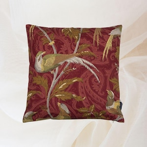 Könnte beinhalten: Quadratisches Zierkissen mit einem bordeauxfarbenen Paisley-Muster und detaillierten Illustrationen von Vögeln auf Ästen mit Blättern. Die Vögel haben grüne, braune und weiße Federn. Auf der Seite befindet sich ein blaues Etikett.