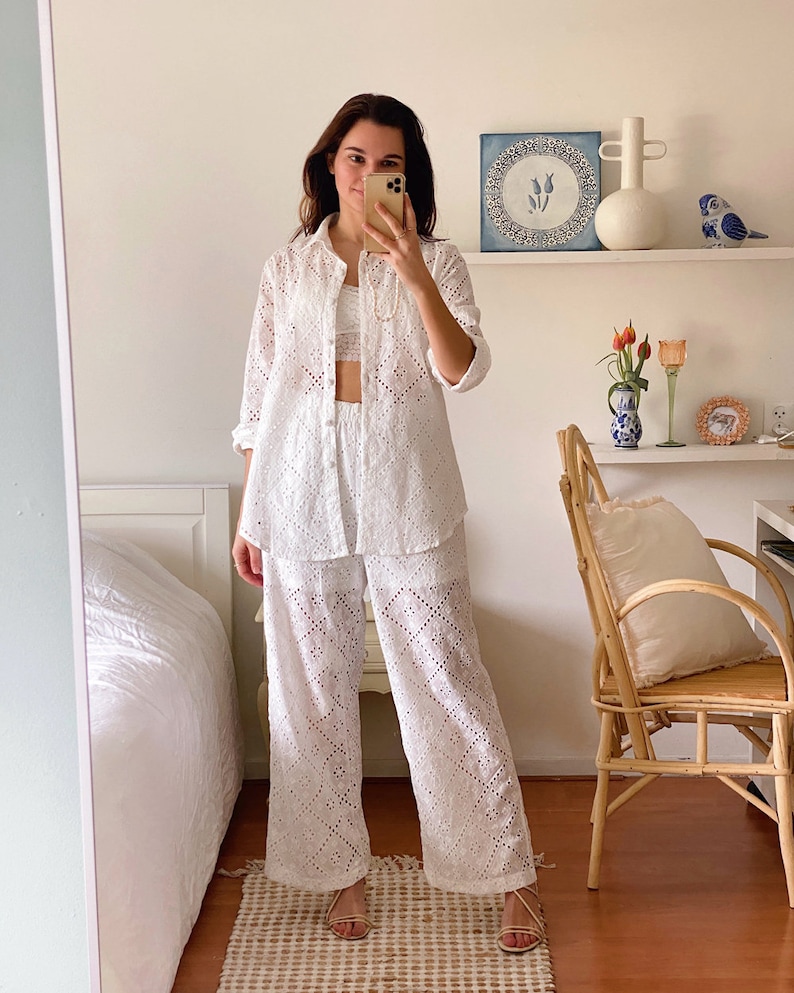 May include: A white eyelet top and pants set with a relaxed fit. The top has a collared neckline and long sleeves. The pants are wide-legged and have a straight leg.
