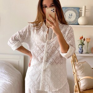 May include: White eyelet cotton pajama set with a long-sleeved shirt and shorts. The shirt has a button-up front and a collar. The shorts have a relaxed fit.