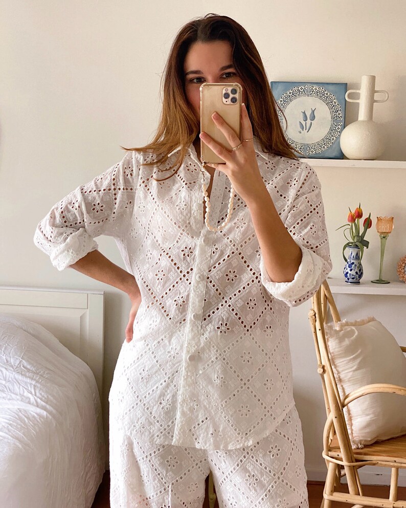 May include: White eyelet cotton pajama set with a long-sleeved shirt and shorts. The shirt has a button-up front and a collar. The shorts have a relaxed fit.