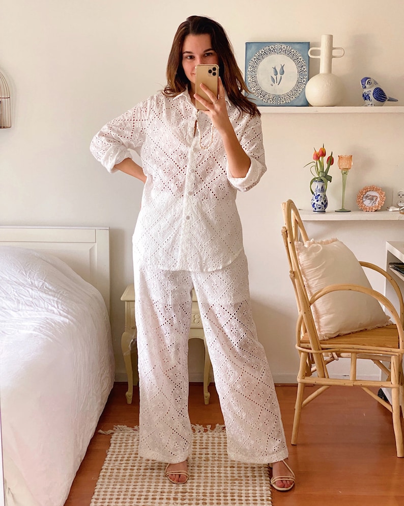 May include: A white eyelet pajama set with a long-sleeved shirt and wide-leg pants. The shirt has a button-up front and a collar. The pants have a relaxed fit.