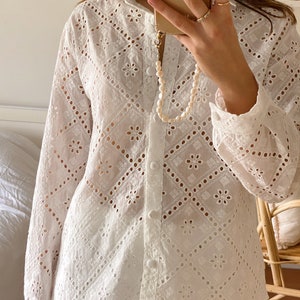 May include: White long-sleeved button-up shirt with a delicate eyelet pattern. The shirt has a relaxed fit and a collar.