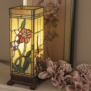 Könnte beinhalten: Eine Tischlampe aus Tiffany-Glas mit einem floralen Design und einer Libelle. Die Lampe hat einen braunen Sockel und einen rechteckigen Schirm.