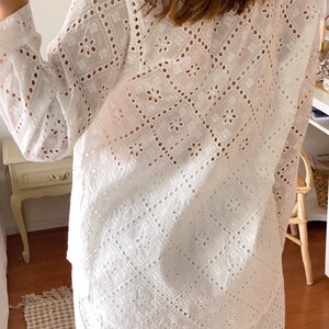 May include: White eyelet top and pants set with a geometric pattern. The top has long sleeves and a button-up front. The pants have a wide leg.
