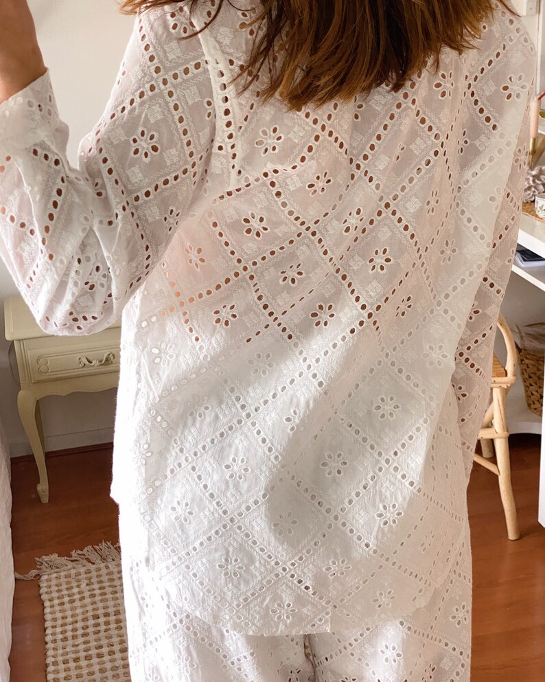 May include: White eyelet top and pants set with a geometric pattern. The top has long sleeves and a button-up front. The pants have a wide leg.