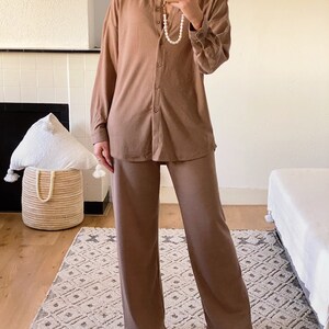 May include: A brown ribbed knit shirt and matching pants set. The shirt has a collared neckline and long sleeves. The pants are wide-legged and have a straight fit.